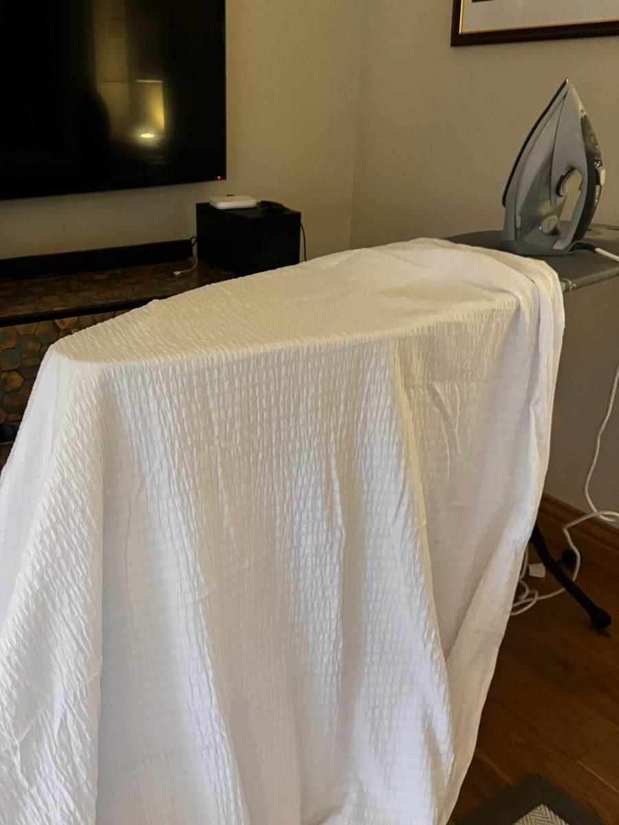 A white sheet draped over a chair to be ironed, an iron waiting behind it