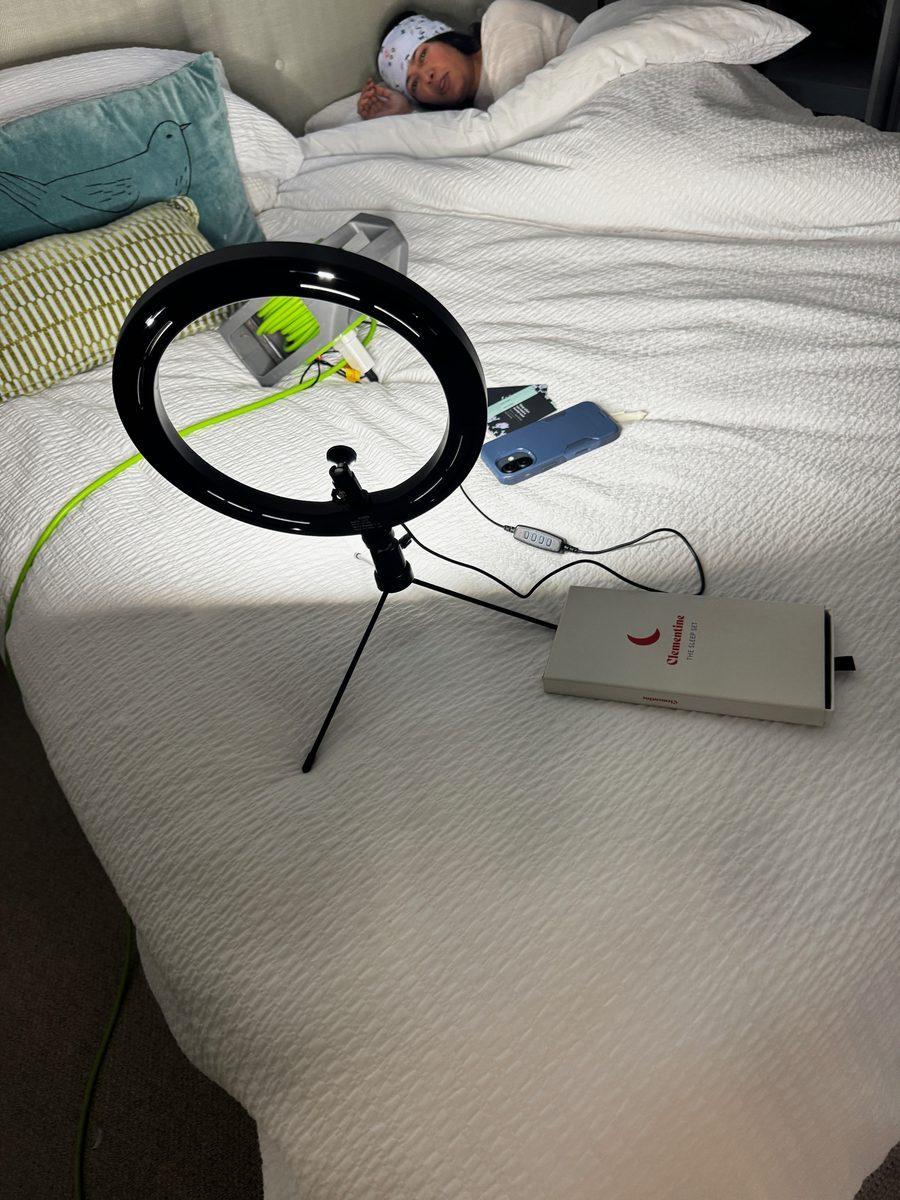 A small ring light on the bed, with a friend asleep in the sleep band and a Clementine box beside her