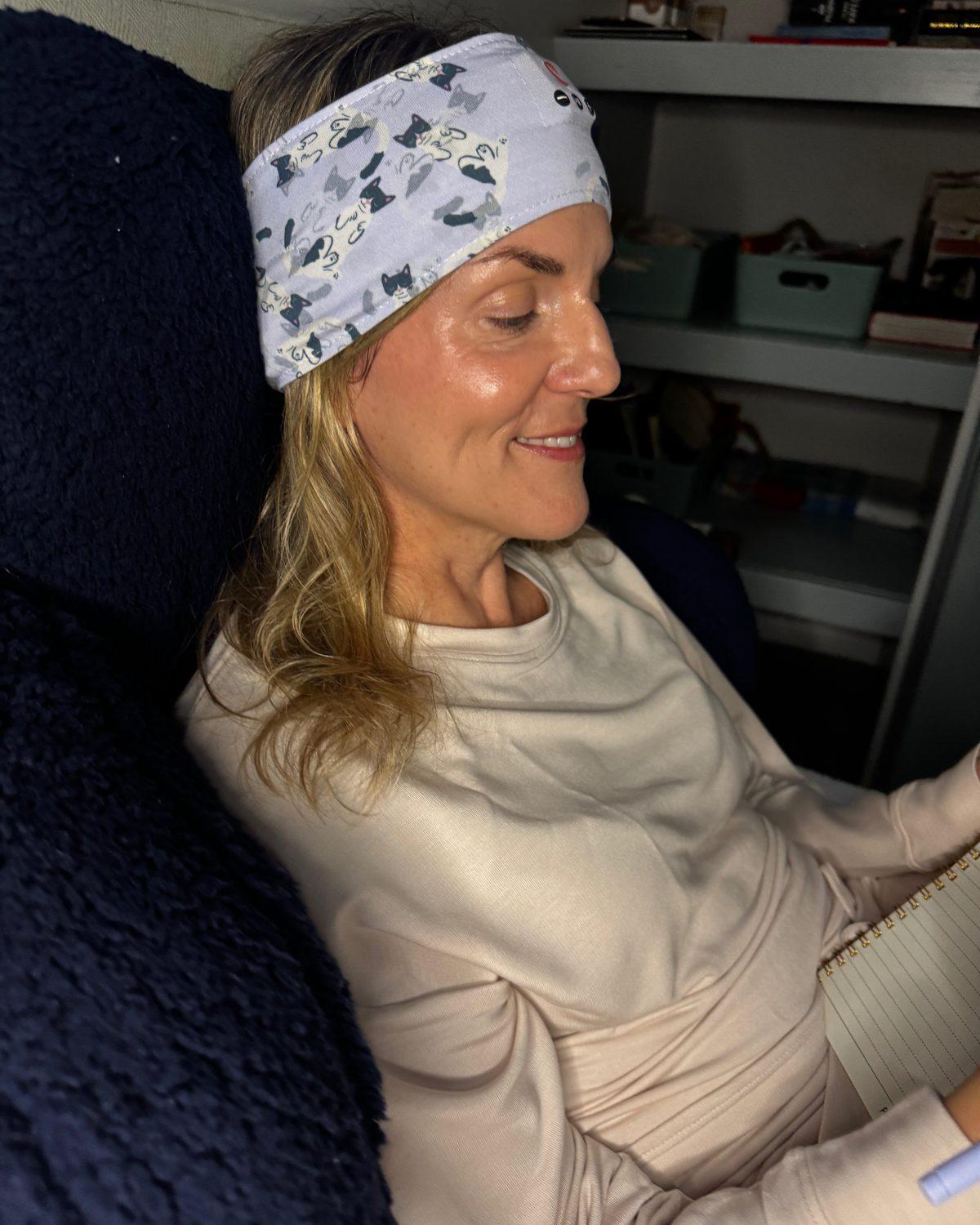 A woman sitting up in bed in the morning, smiling, still wearing the Clementine sleep band