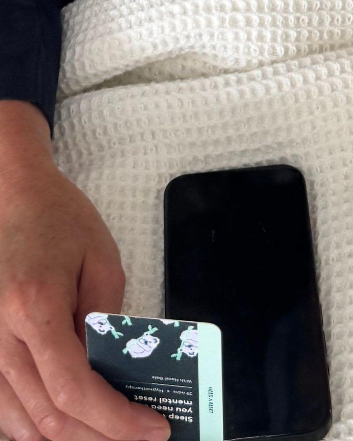 A woman in bed tapping a sleep ritual card against the back of her phone
