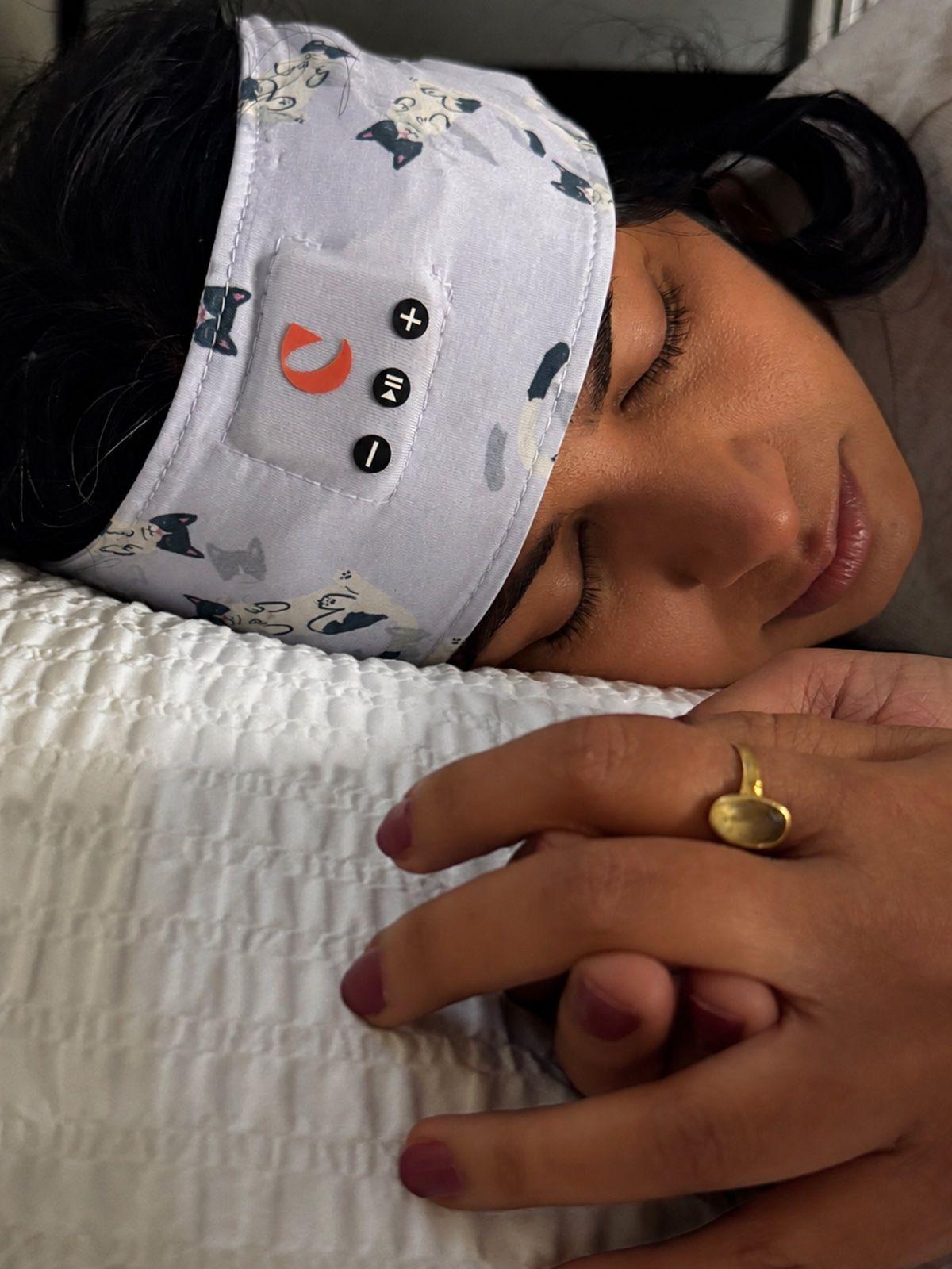 A woman asleep on her side on a white pillow, wearing the Clementine sleep headband