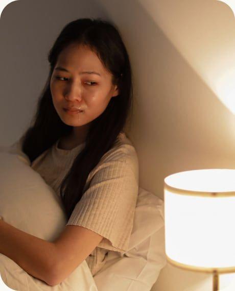 A woman sitting up in bed by lamplight