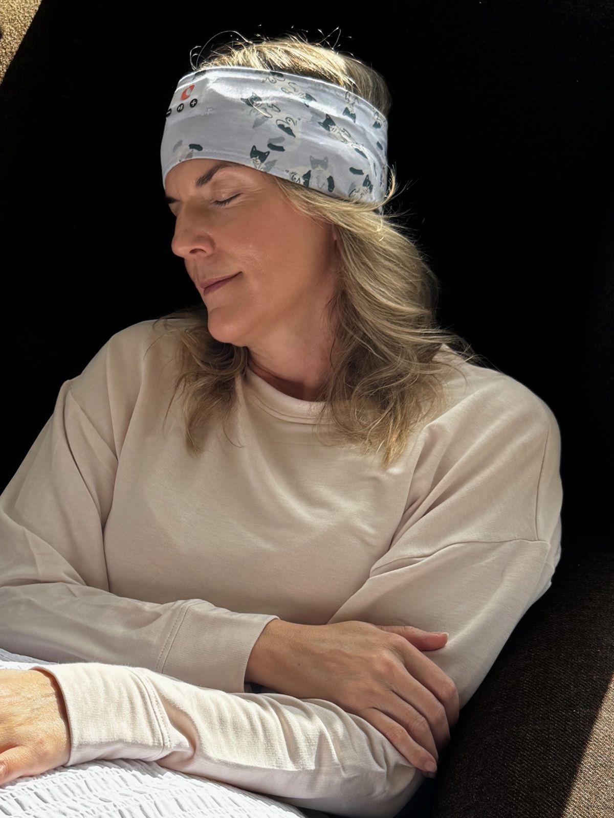 A woman with her eyes closed in an armchair, wearing the Clementine sleep headband