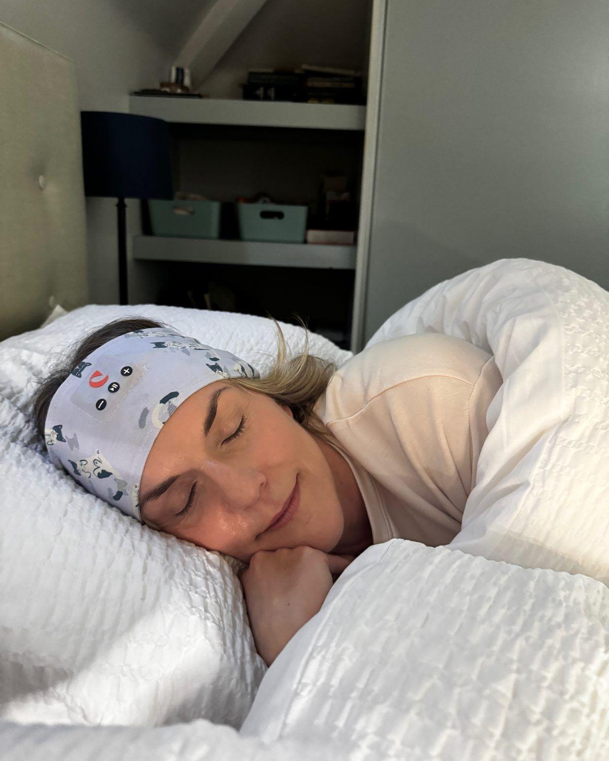 A woman asleep on her side in bed, wearing the Clementine sleep band